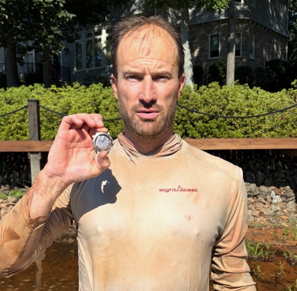 Phil, mud-stained from the dive, holding up a recovered dive watch at the Lake Norman shoreline
